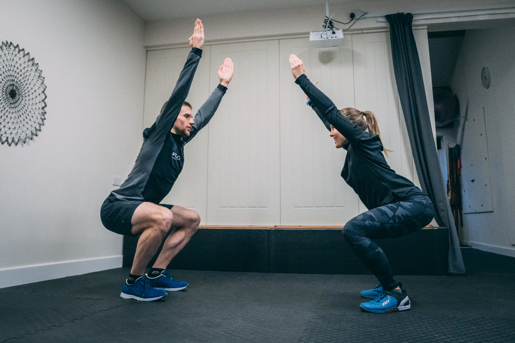 A male and female athlete holding a squat position facing each other during a strength training session for runners.