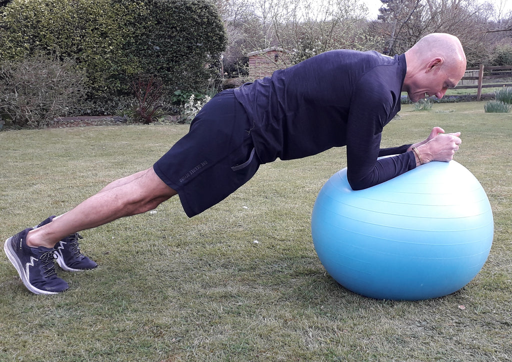 A male runner holds a plank position balancing on a blue swiss ball