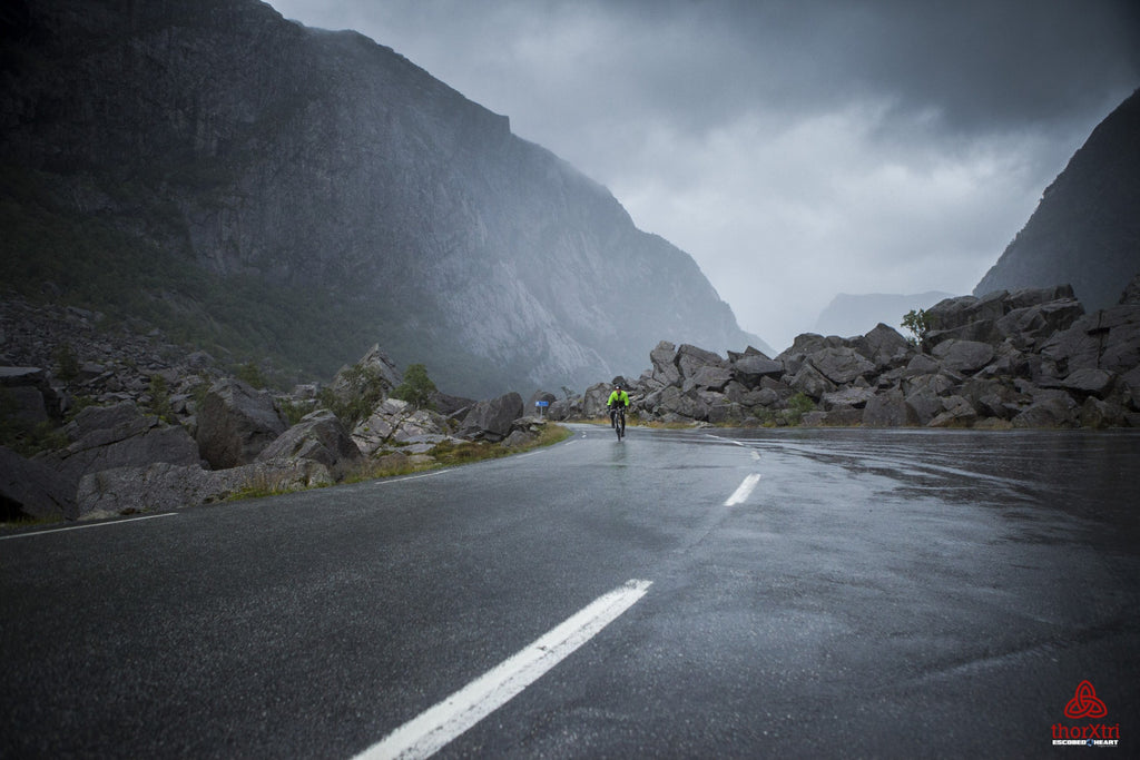 A lone cyclist rides through a misty and rocky mountain pass in Norway during the Thorxtri