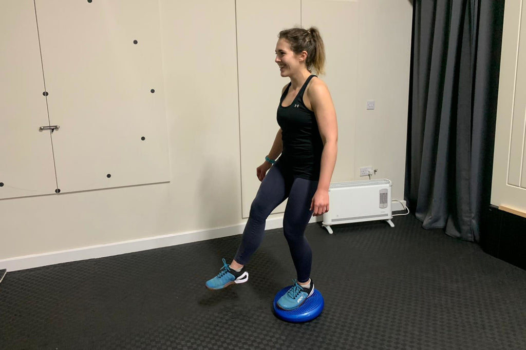 A female runner standing on one leg on a wobble cushion to improve balance and lower leg conditioning
