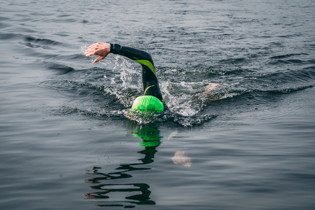 A triathlete wearing a green swimming cap swims towards the camera
