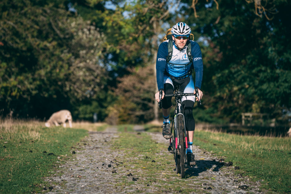 Male gravel rider cycling on a grassy gravel road with a sheep in the background