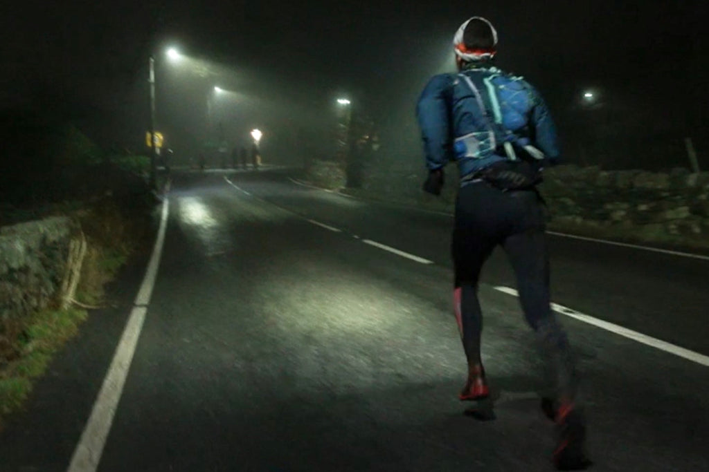 A male runner heading along a dark section of road with a head torch lighting the way