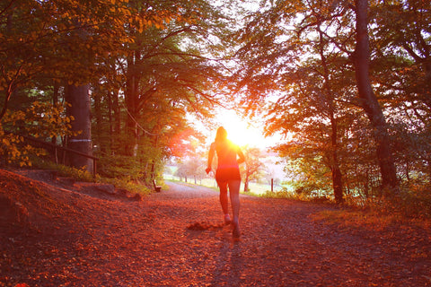 A female runner heading out of a forest into a brilliant orange and red sunset
