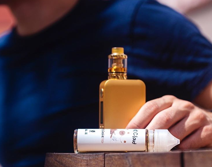 a close-up shot of a man holding his gold vaping mod close to a bottle of Velvet Cloud e-liquid