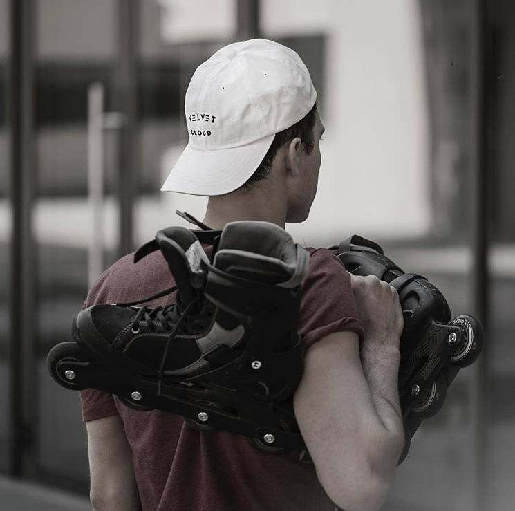 a man wearing a Velvet Cloud hat holding skates over his shoulder