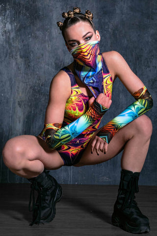 A woman in squat position wearing rave outfit with festival neck gaiter.