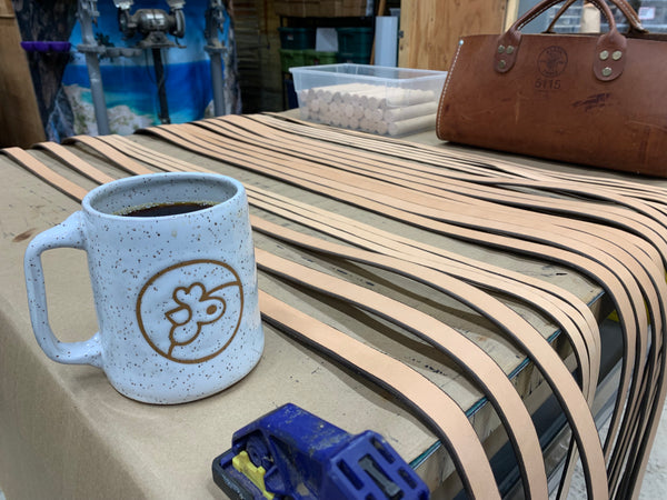 Handmade Mug with Artisans Cooperative Logo in Glaze on Workbench with Leather Straps and Lineman's Bag in Walnut Workshop