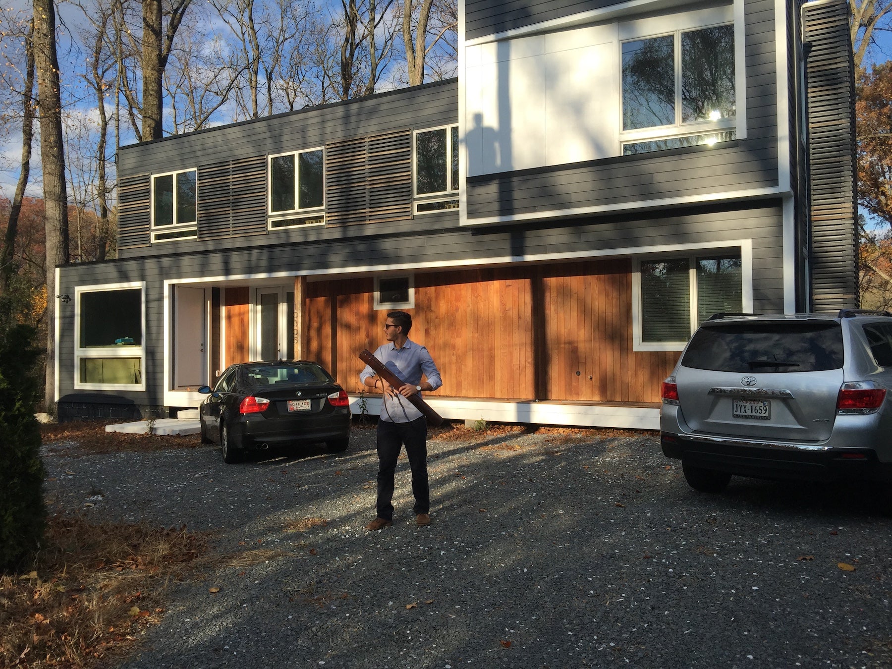 A man walking away from a beautiful custom new built house holding a leather blueprint tube