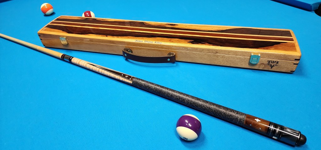 Leather handle on custom wood pool cue case on the blue pool table felt surface, with a pool stick and four pool balls. 