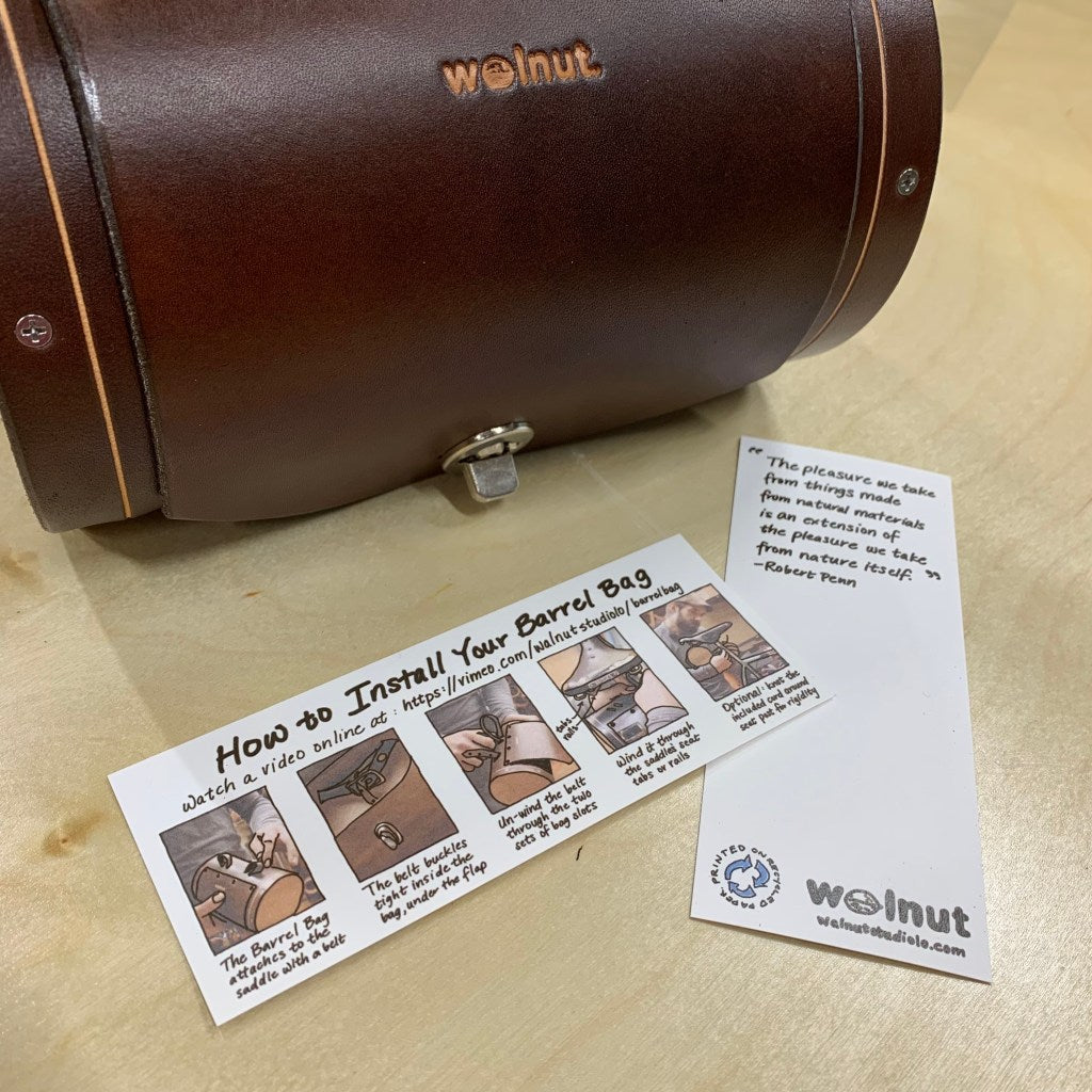 Dark Brown Bicycle Barrel Bag Shown with Installation Guide Bookmark on Table