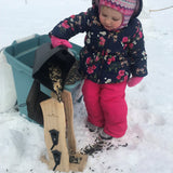 toddler girl filling bird feeder in snow