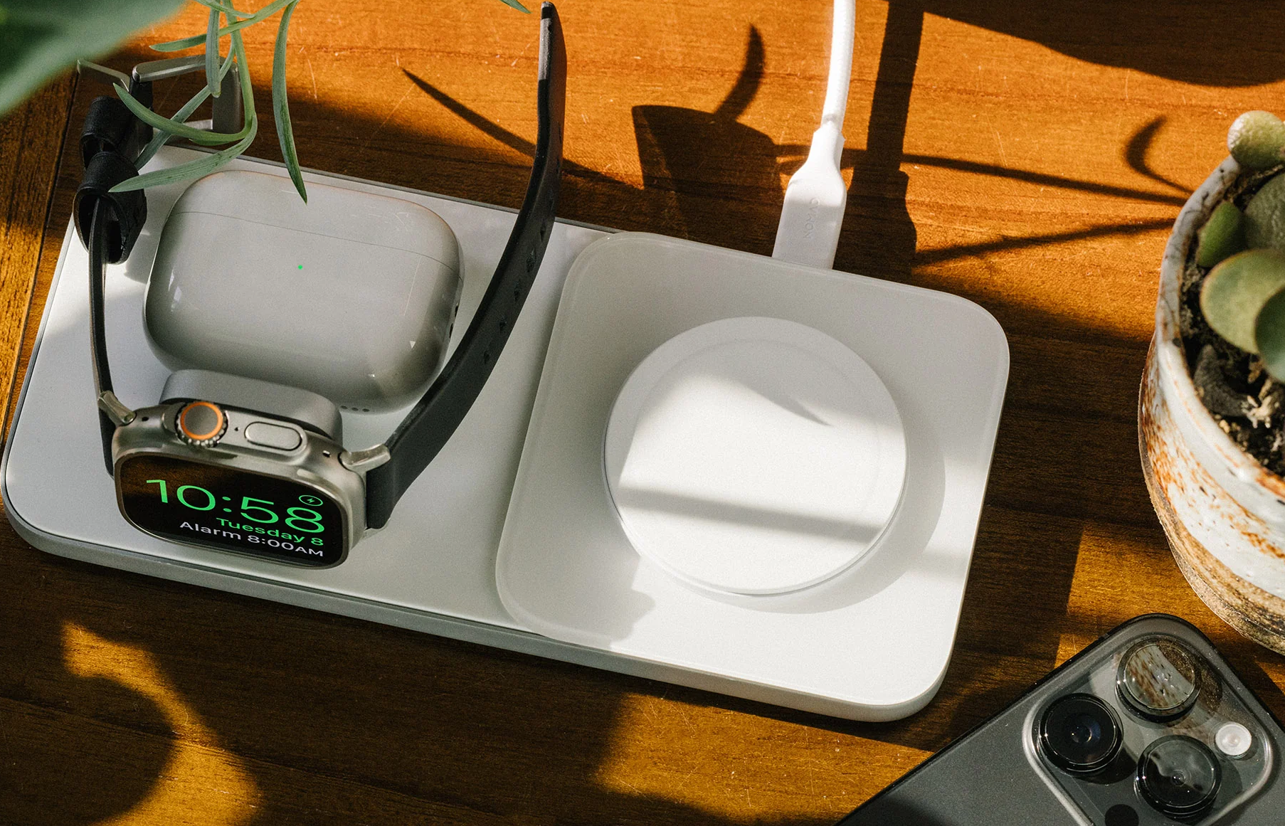 Nomad Base One Max Wireless Charger for 3 Apple devices in one on the table close to a plant and computer