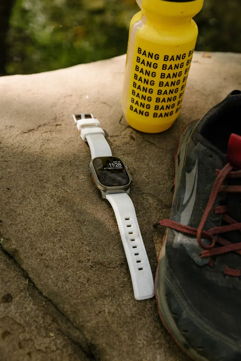 A bottle, apple watch and a pair of running shoes captured laying on the grass