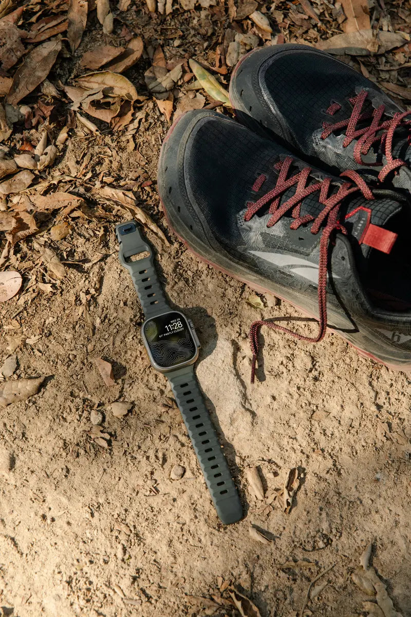 An apple watch and a pair of running shoes are captured laying on the grass