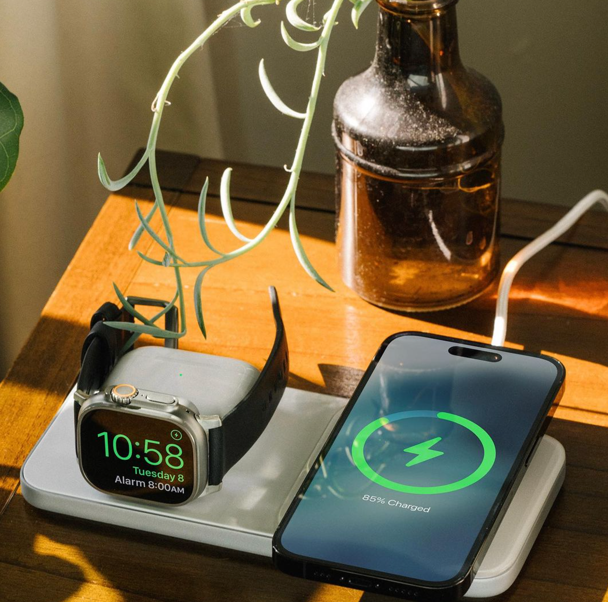 Nomad Base One Max charger in colour silver on the bedside table charging an iPhone, Apple Watch and AirPods