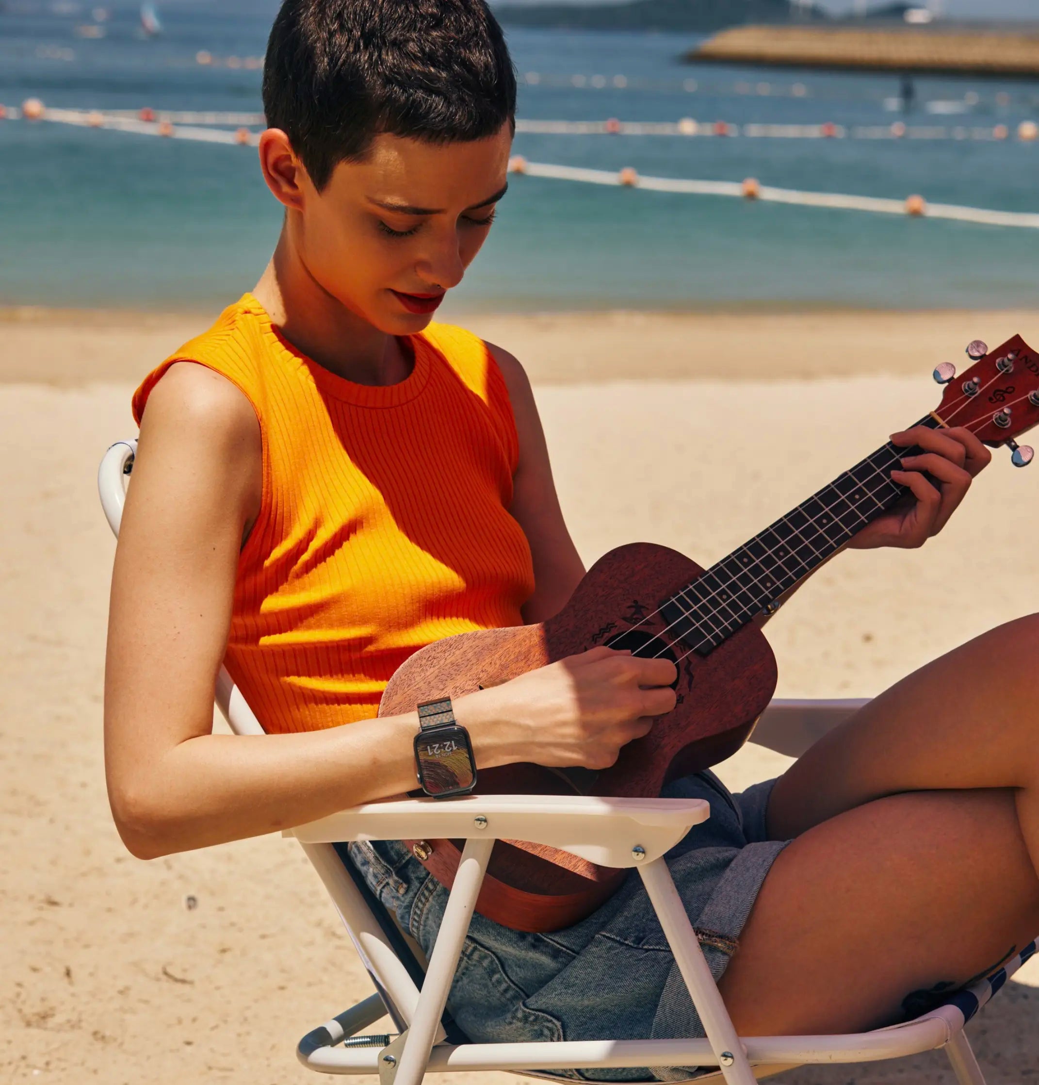 A girl sitting on a beach playing a musical instrument with PITAKA Apple watch band on her wrist