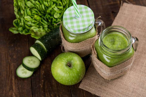 Two mason jars of green juice beside an apple and cucumber