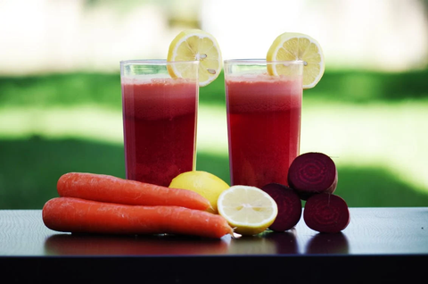 A fresh juice beside carrots, lemon, and beet