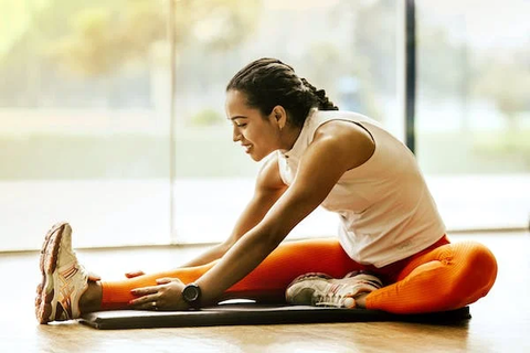 A woman wearing orange pants and a white shirt, stretching