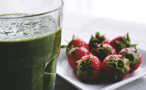 A green smoothie next to a plate of strawberries