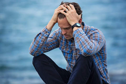 A man in a blue and brown plaid shirt, with his hands in his hair