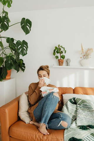 A woman sitting on an orange couch, blowing her nose