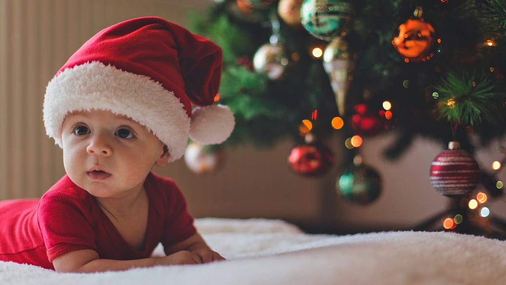 Baby mit Weihnachtsmütze vor geschmücktem Weihnachtsbaum