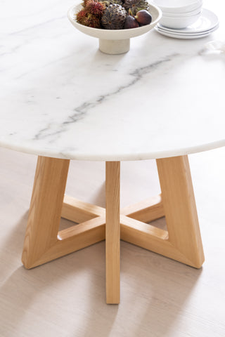 Italian Marble Round dining table from The Loom Collection furniture shop in Dubai, with light wood legs and a grey veining. The Table has a bowl of fruits on top and a few dining accessories for design flair.