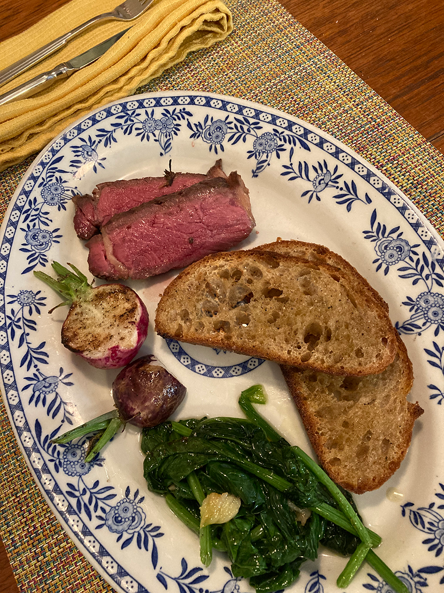 a couple slices of medium buffalo bone-in ribeye with crustinis and vegetables on decorative plate