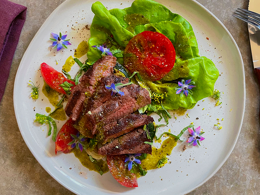 overhead shot of a buffalo steak salad with butter lettuce and garden tomatoes