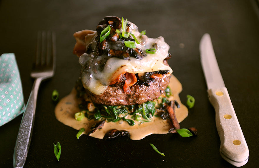 Bison burger patty topped with bacon, mushroom, and Swiss cheese placed over creamed spinach.