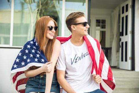 girl and guy wearing US flag cape both wearing wooden sunglasses