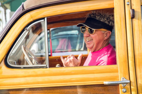 man in pink shirt wearing sunglasses driving a vintage wagon