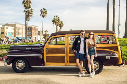 couple standing on the side on their vintage wagon both wearing sunglasses