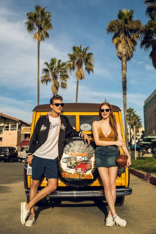 couple standing behind their vintage wagon both wearing sunglasses