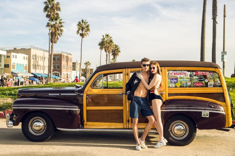 couple hugging standing on the side on their vintage wagon both wearing sunglasses