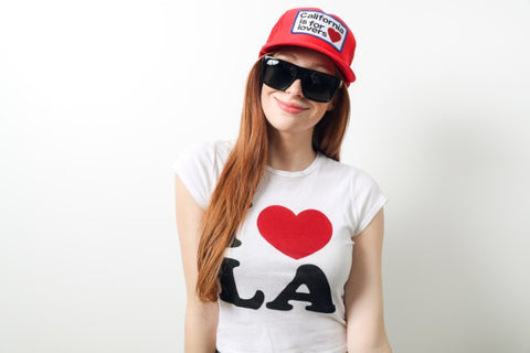 girl wearing red cap that says California is for lovers in a white top that says I love LA wearing a black sunglasses