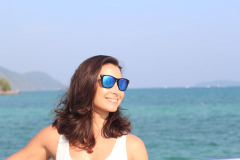 girl in white tank top wearing blue sunglasses smiling for a camera shot