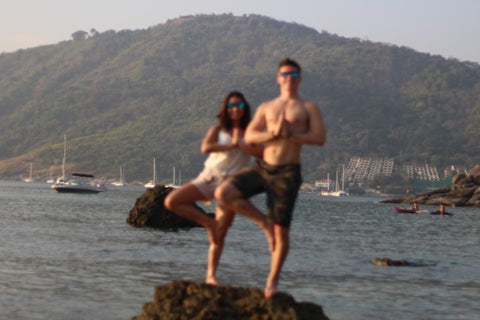 guy and girl wearing sunglasses doing a yoga pose on a rock