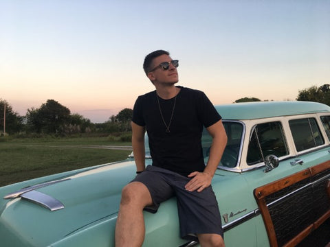 guy wearing a sunglasses sitting on the hood of a vintage car