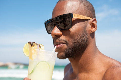 guy wearing wooden sunglasses having a drink at the beach