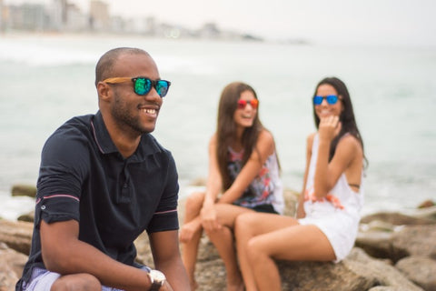 guy in dark blue polo shirt wearing a sunglasses in the shade of bluish green with his 2 girl friends behind him