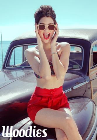 girl in floral top and red shorts sitting on a vintage car's hood wearing wood sunglasses 