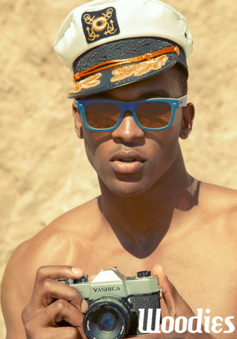 topless guy wearing captain's hat in blue sunglasses holding a camera