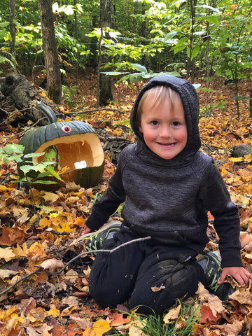A little boy having fun in the wood's with a carved pumpkin.