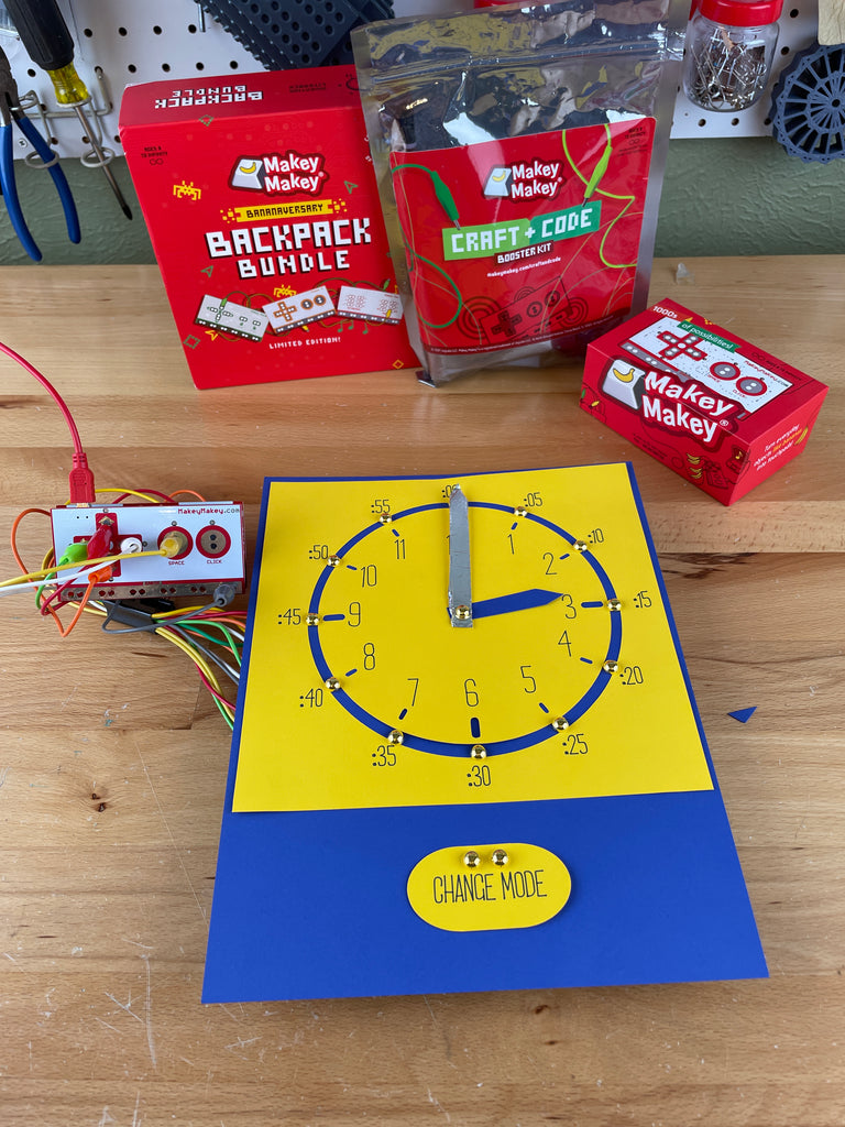 Makey Makey Kit with paper clock. Clock hands are made of foil and there are brass fasteners at 12,3,6,9 so Makey Makey can tell the time.