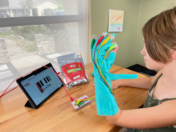 Young girl  with hand in glove with thumb exposed. She touches fingertip to thumb to play piano on tablet.