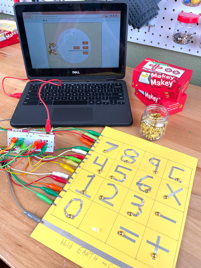Paper Calculator connected to Makey Makey and a computer displaying a Scratch project.