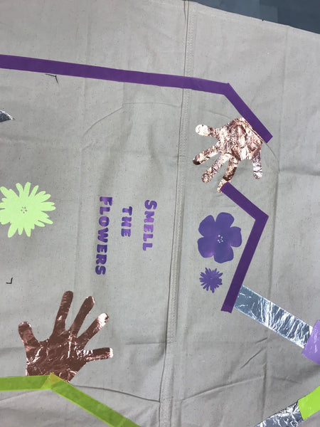 Tarp with tape maze, hand print, and vinyl cut flowers. Text says "Smell the flowers"